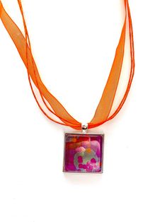 a necklace with an orange ribbon around it and a square pendant hanging from the front