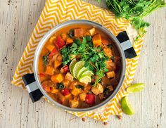 a bowl of soup on a yellow and white napkin next to cilantro, avocado and lime