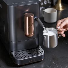 a woman is filling a cup with milk from a coffee maker on a countertop