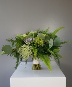 a bouquet of greenery is sitting on a white box against a gray wall,