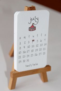 a small wooden easel with a calendar on it's side and an image of a tent in the background