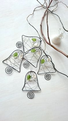 four metal bells with green leaves and pearls hanging from the sides on a white table