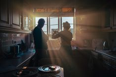 two people standing in a kitchen with sunlight coming through the window and on the counter