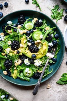 a green salad with blackberries and cucumbers in it on a blue plate