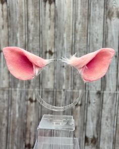 a pink cat ears headband with white feathers on top of a clear acrylic stand