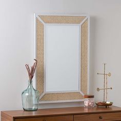 a white framed mirror sitting on top of a wooden dresser next to a vase with flowers