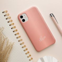 a pink phone case sitting on top of a desk next to a pen and notebook