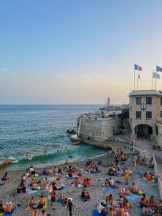 many people are sitting on the beach near the water and in front of an old building