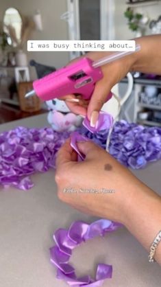 a woman is using a pink device to cut purple ribbon on a table with flowers