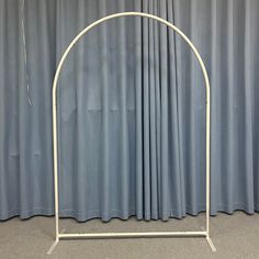 a white metal arch stands in front of a curtained wall with blue drapes