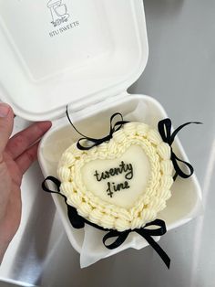 a heart shaped cake in a white container with black ribbon around the edges and writing on it