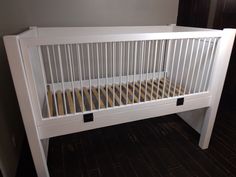 a white crib with wooden slats in the corner and wood flooring on the other side