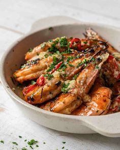 a white bowl filled with cooked shrimp and garnished with herbs