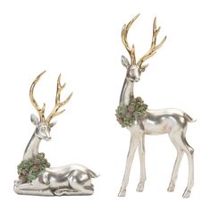 two silver deer figurines with pine cones on their antlers, one laying down