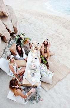 a group of women sitting on top of a beach next to each other eating food