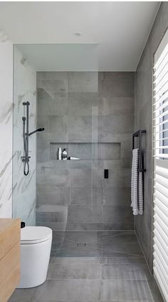 a bathroom with a toilet, shower and window coverings in shades of light gray