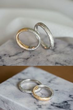 two silver and gold rings sitting on top of a marble block