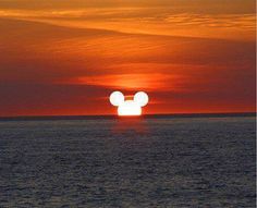 the sun is setting over the ocean with mickey mouse silhouettes