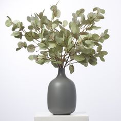 a gray vase filled with green leaves on top of a white countertop next to a wall