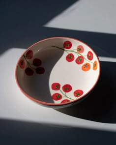 a bowl with red flowers painted on it sitting on a white counter top next to a shadow