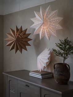 three paper snowflakes hang from the ceiling above a table with books and a potted plant