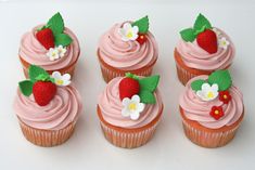 four cupcakes with pink frosting and strawberries on top are arranged in a row