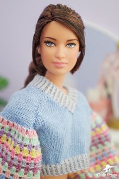 a doll wearing a blue sweater with multicolored crochet