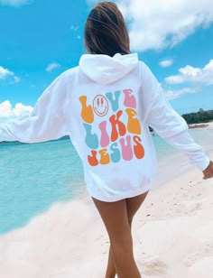 a woman walking on the beach wearing a white hoodie