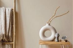 a white vase sitting on top of a wooden table next to a purple painted wall