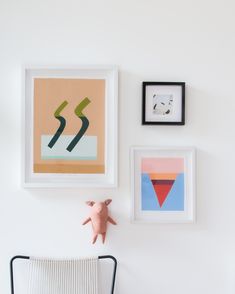 three framed art pieces hang on the wall above a chair with a stuffed animal in front of it