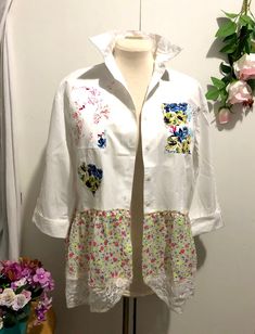 a white shirt with colorful flowers on it and a pink flower pot in the background