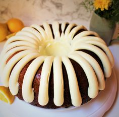 a bundt cake with white icing on a plate next to some lemons