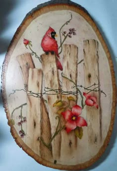 a red bird sitting on top of a wooden fence with flowers painted on it's side