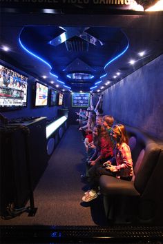 kids are sitting on the couch watching televisions in a video game room with blue lighting