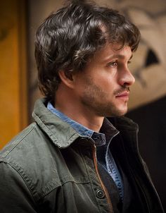 a man with curly hair wearing a jacket and looking off to the side in front of a clock