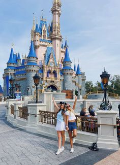 two women standing in front of a castle at disney world with their arms raised up