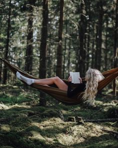 a woman is sitting in a hammock reading a book and drinking coffee while holding a mug