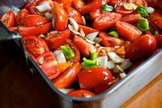 a metal pan filled with lots of tomatoes and onions on top of a wooden table