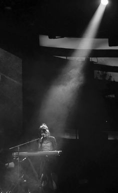 a woman standing in front of a microphone on top of a stage with light coming from behind her