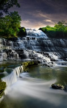 a waterfall is shown at night with stars in the sky and water flowing over it