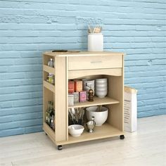 a small wooden cabinet with shelves and bowls on wheels in front of a blue brick wall