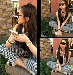 a woman sitting on the ground looking at her cell phone while wearing sunglasses and checkered pants