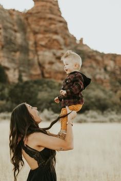 a woman holding a baby up in the air while standing on top of a field