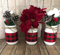 three mason jars decorated with poinsettis and pine cones