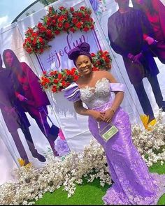 a woman standing in front of a sign with flowers on it and wearing a purple dress