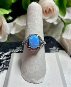 Simulated Blue Fire Opal Vintage Style Ring Custom/Made To Order  Inspired by the Victorian style, I now offer this filigree ring in antiqued sterling silver. The beautiful oval cut gemstone is 10mm by 8mm... This ring is 13mm NS (North/South) on the finger. The inside of the band is marked 925 for sterling. Notice the beautiful detailed flower dainty craftsmanship of the silver setting. This lovely ring stands out and illuminates the finger with its great shine. This is an exquisite rendition of an antique filigree ring.... and is ready to wear. Sincerely Jane A collection supported by Silver Embrace Jewelry INTERNATIONAL SHIPPING: First Class International or Priority Mail International RETURNS & Exchanges accepted with in 30 after arrival Visit our Etsy Shop Here:   https://silverembrac Blue Opal Jewelry For Anniversary, Adjustable Blue Opal Ring, Adjustable Blue Jewelry With Accent Stones, Vintage Style Blue Opal Ring Gift, Vintage Blue Opal Ring For Gift, Vintage Blue Opal Ring Gift, Ornate Blue Oval Jewelry, Adjustable Blue Opal Gemstone Ring, Blue Opal Spiritual Ring For Gift