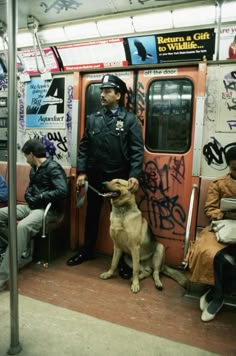 a man in uniform standing next to a dog on a subway train with graffiti all over the walls