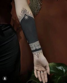 a woman's arm with tattoos on it and a plant in the foreground