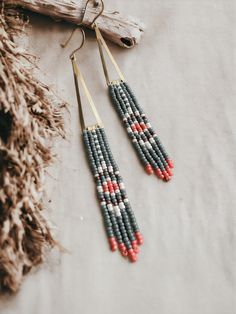 two pairs of beaded earrings hanging from a piece of driftwood on a table