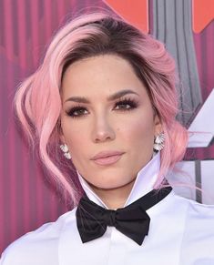 a woman with pink hair wearing a white shirt and black bow tie at an event